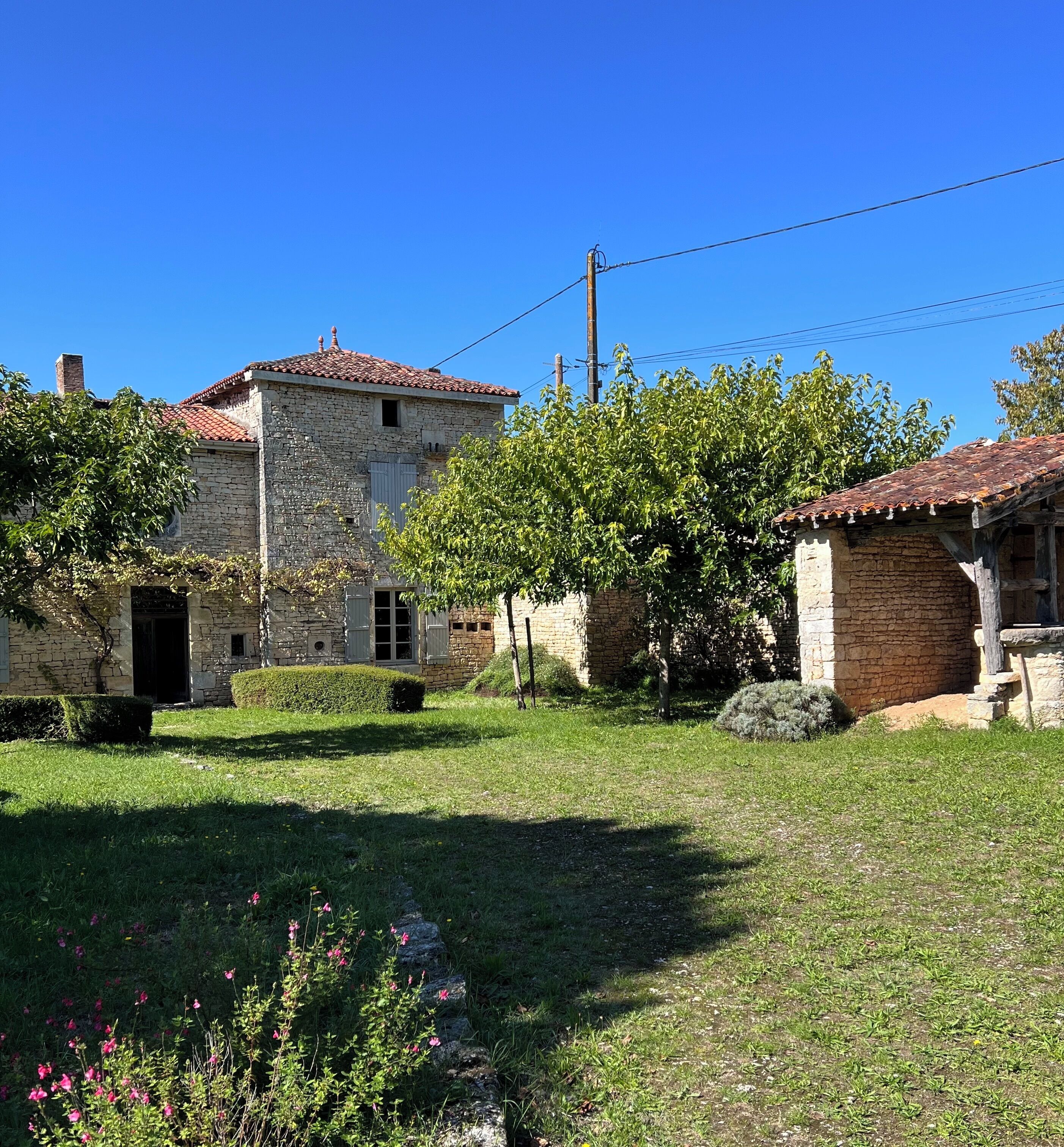 A stone building with a tiled roof, surrounded by a well-maintained garden with grass and flowering plants.