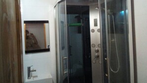 A corner bathroom with a glass-enclosed shower stall, a sink, and a framed picture on the wall.