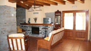A cozy living room with a stone fireplace, wooden furniture, and a television. - Rural house (full rental) El Racó de Cal Maró for 10 persons (Montferrer i Castellbò)