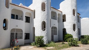 A white building with multiple arched windows and balconies, surrounded by greenery.
