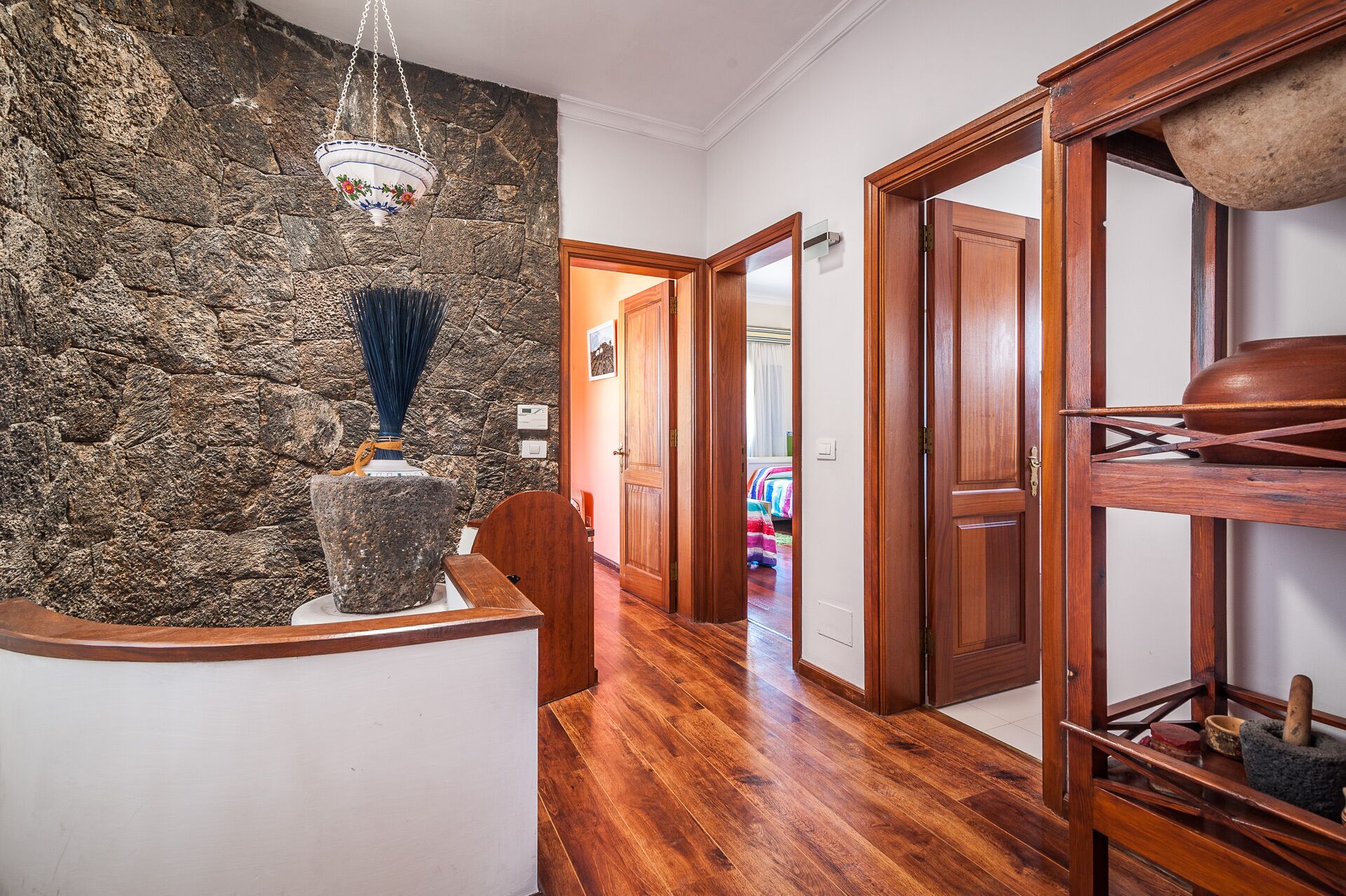 A hallway with a stone wall, wooden floor, and a rustic wooden shelf with a mortar and pestle.