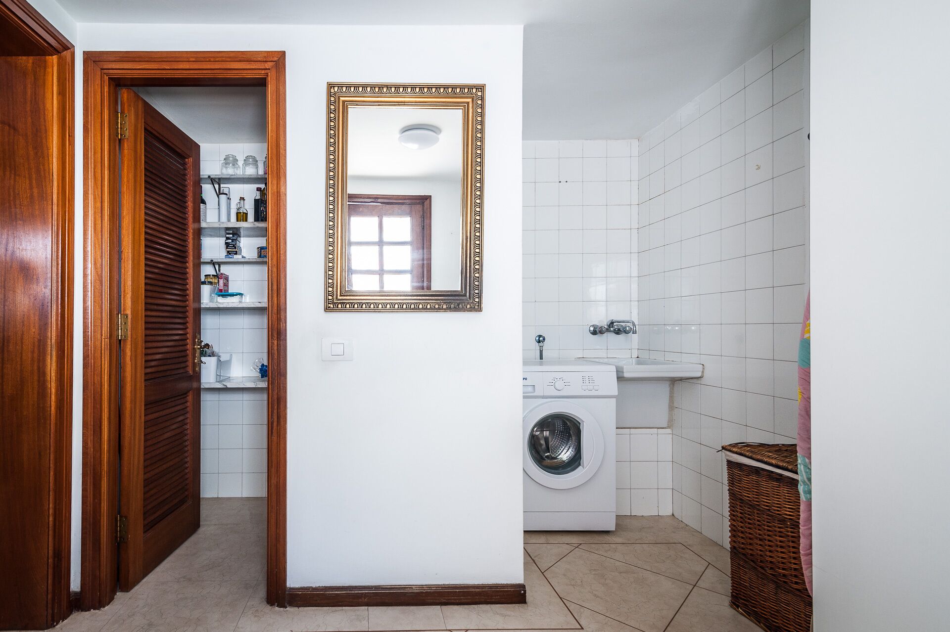 A laundry room with a washing machine, a sink, and a mirror on the wall.