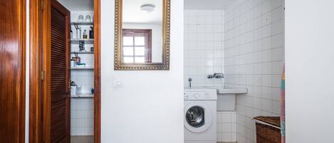 A laundry room with a washing machine, a sink, and a mirror on the wall.