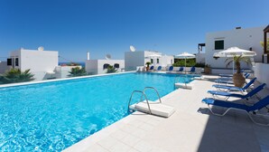 A swimming pool with blue water, surrounded by white buildings and blue lounge chairs. - Island-style 3 bedroom house!  (Rethymno)