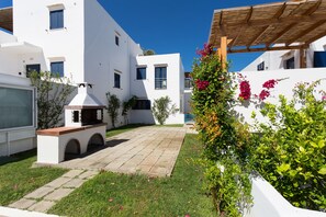 A courtyard with a stone pathway, white buildings, and a pergola.