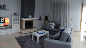 A modern living room with a grey sofa, a small white coffee table, a fireplace, and a television on a stand. - Beach, valley and relaxation (Pontevedra)
