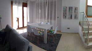 A modern living room with a grey sofa, a dining table with chairs, a staircase with glass railings, and a small wooden cabinet. - Beach, valley and relaxation (Pontevedra)