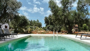 Una piscina cristalina con sillones de descanso y una estructura de madera en un jardín ajardinado.