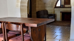 Un comedor con mesa y sillas de madera, arcos de piedra y una chimenea al fondo.
