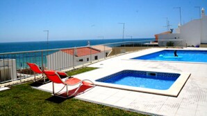 A rooftop pool area with two pools, a red chair, and a view of the sea.