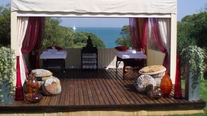 A wooden deck with a white canopy, towels, and spa items, overlooking a scenic view.
