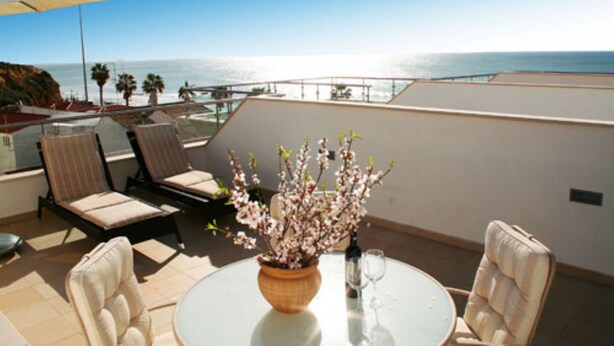 A terrace with a table, chairs, a vase of flowers, and a view of the sea.