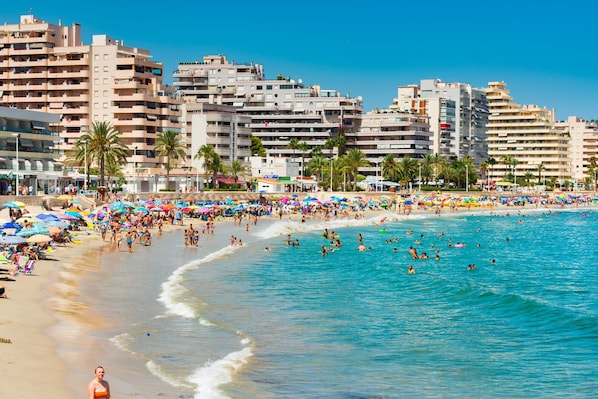 Une plage bondée où l’on voit des gens nager et bronzer, le tout entouré de grands immeubles.