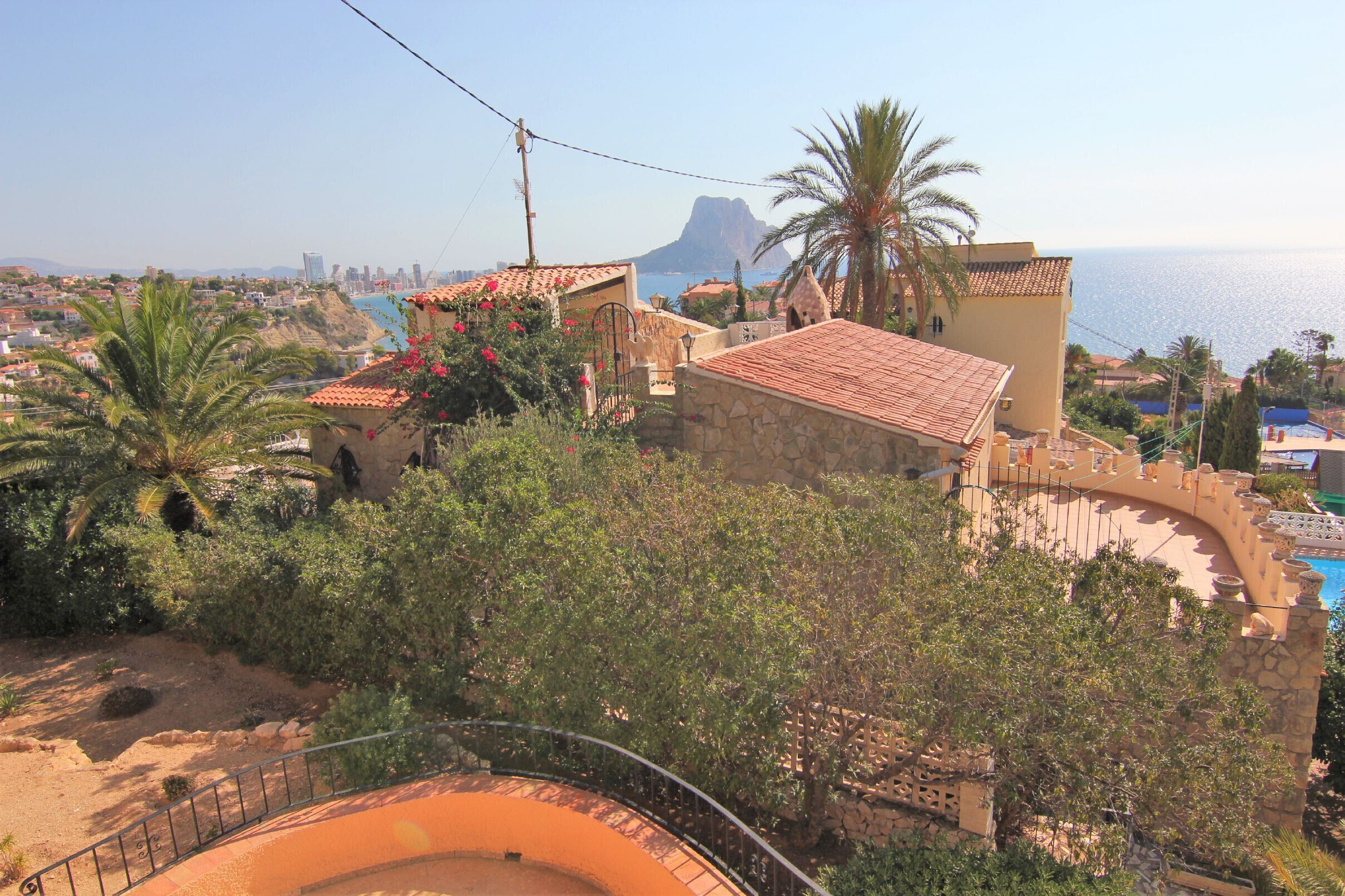 A coastal villa with a stone facade, a curved swimming pool, and a view of the sea and city skyline.
