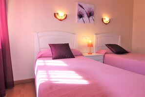 Quarto de hotel com duas camas, cada uma com cabeceira, mesa de cabeceira com abajur e arandelas na parede.
