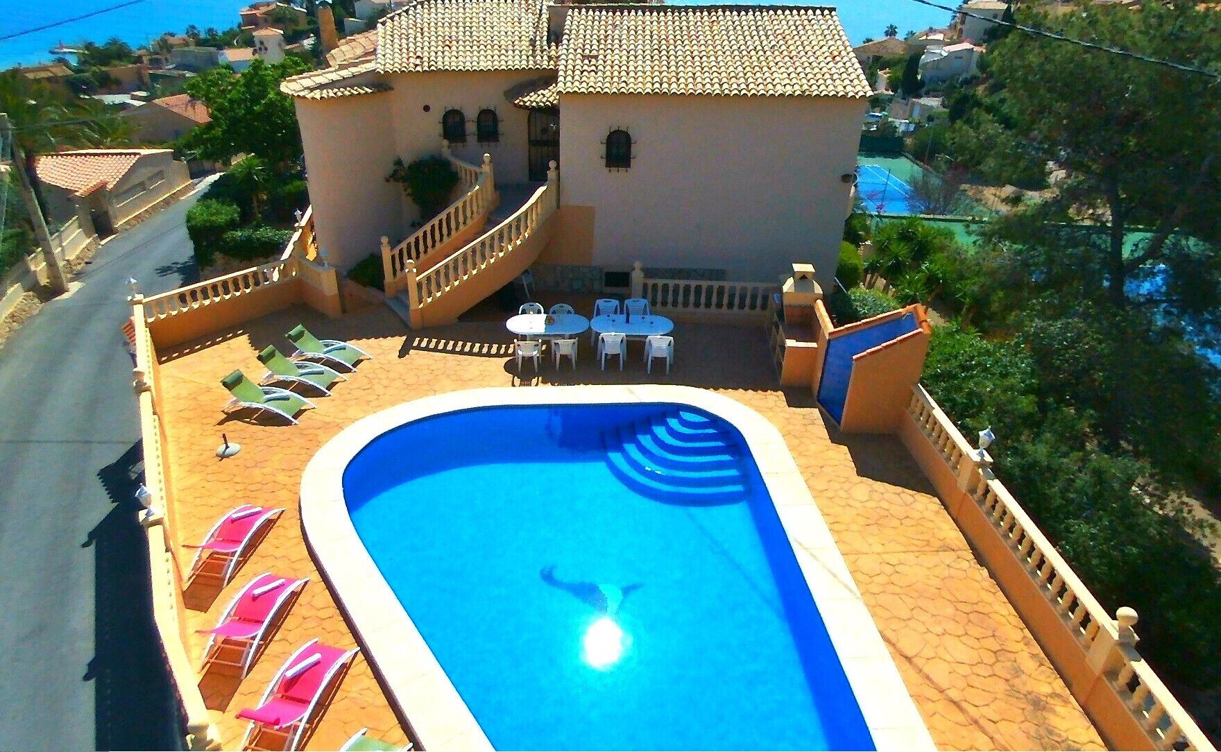 A swimming pool with a sunken center, surrounded by lounge chairs and tables, with a building in the background.