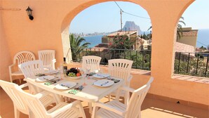 A terrace with a table set for four, white plastic chairs, and a view of the sea and city skyline.