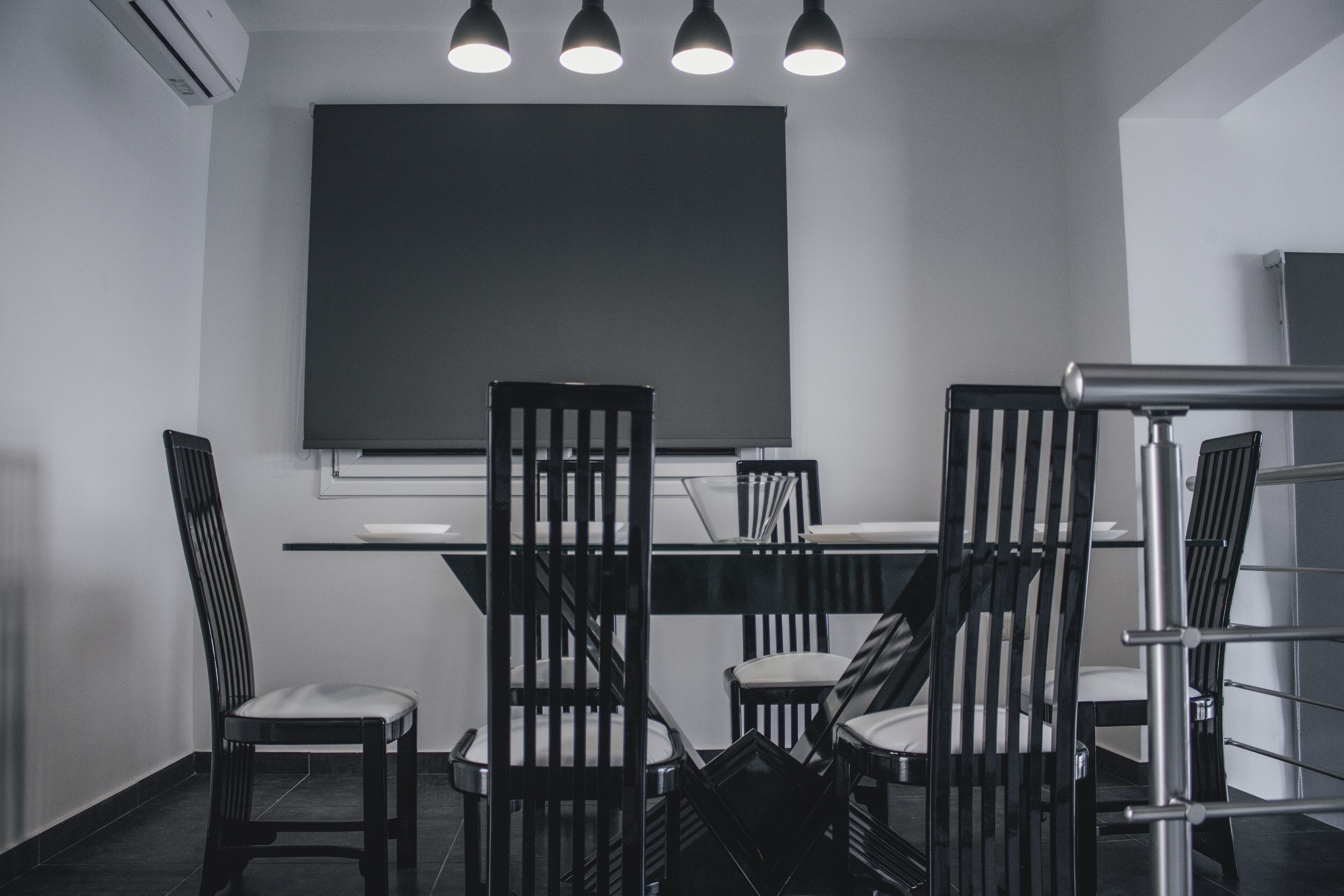 A conference room with a large table, four chairs, a projector screen, and a staircase.