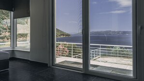 Et moderne værelse med store skydedøre, der fører ud til en balkon med udsigt over hav og bakker.