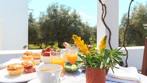 Ein Frühstückstisch mit Gebäck, Früchten und Getränken unter einer Pergola mit Blick auf Bäume.