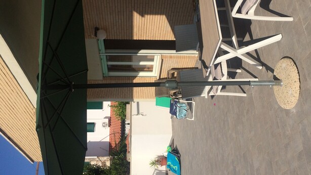 Een terras met een tafel en stoelen, een ronde tafel en een groene parasol.