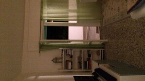 Een kleine kamer met een raam, een radiator en een plank met boeken.
