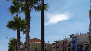 A sunny urban street with palm trees, benches, and colorful buildings. - House very close to beach, family, quiet, clean, air cond., Bright and fresh (La Vila Joiosa/Villajoyosa)