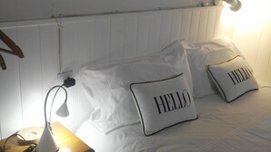 A neatly made bed with two pillows, one with "HELLO" on it, a bedside lamp, a wooden nightstand, and a wall-mounted light fixture. - House very close to beach, family, quiet, clean, air cond., Bright and fresh (La Vila Joiosa/Villajoyosa)