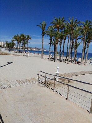 A beach with palm trees, a wooden boardwalk, and a clear blue sky.