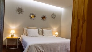 A neatly made bed with white linens and two bedside lamps, a wooden nightstand, and three wall-mounted mirrors. - Entire house for 5 people, private pool, pets accepted. Fully equipped. (Cabeceira de Basto)