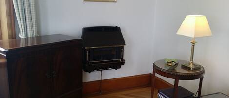 A room with a wooden cabinet, a black fireplace, a small round table with a lamp, and a chair.