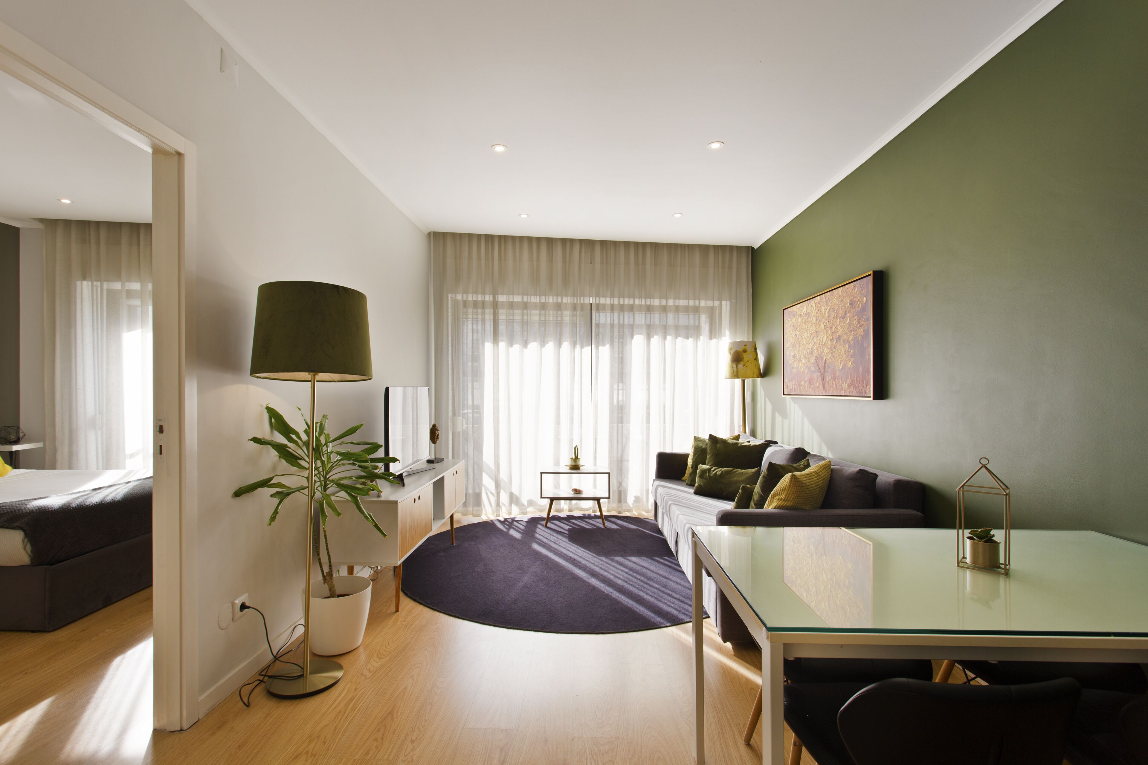 A modern living room with a glass dining table, a sofa, a coffee table, and a potted plant.