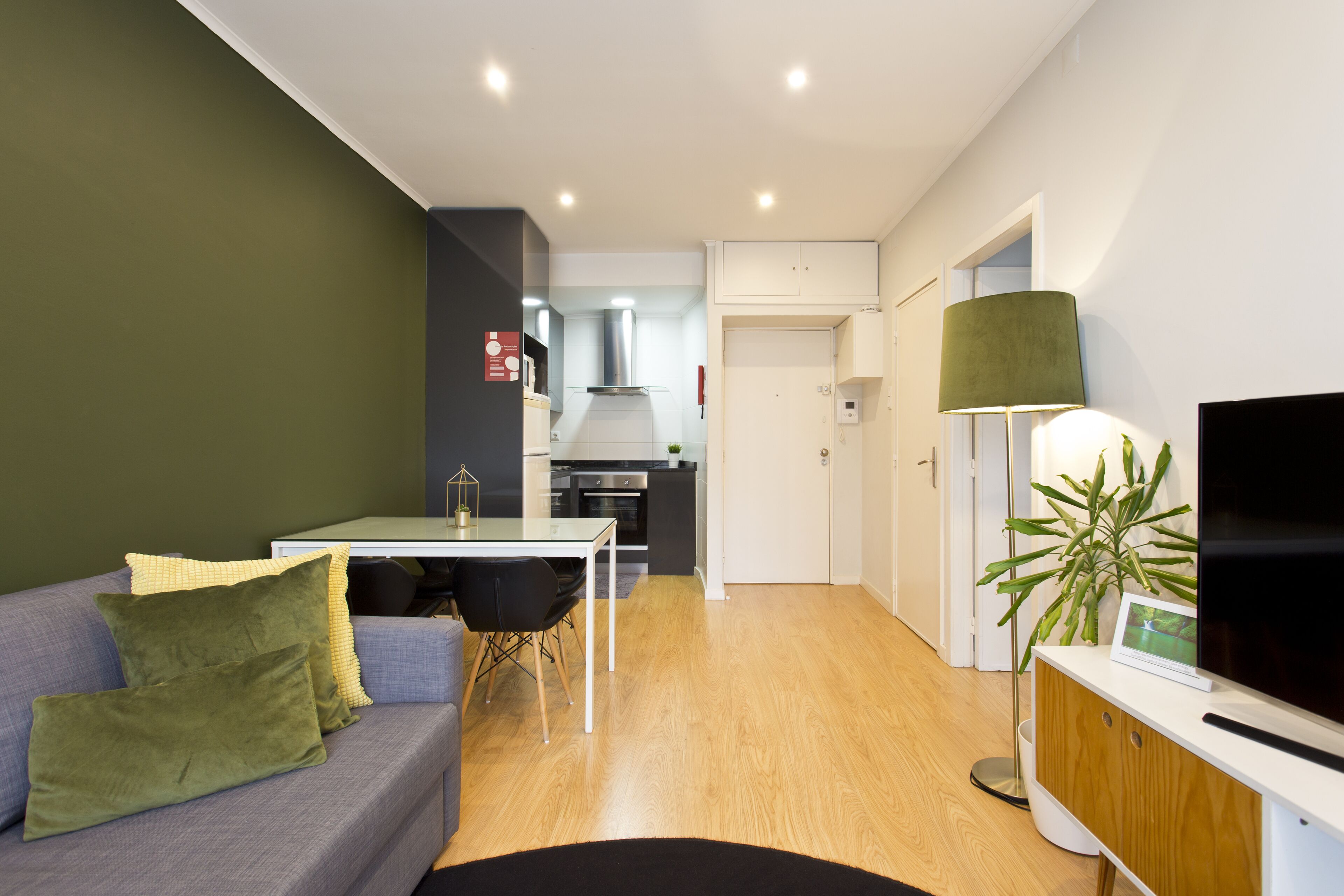 Una sala de estar moderna con un sofá gris, una mesa de comedor y un televisor sobre un mueble de madera.