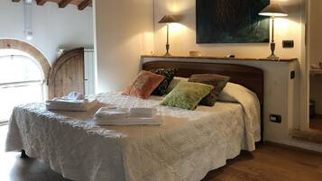 Een slaapkamer met een bed, kussens, een nachtkastje, een lamp en een schilderij aan de muur.
