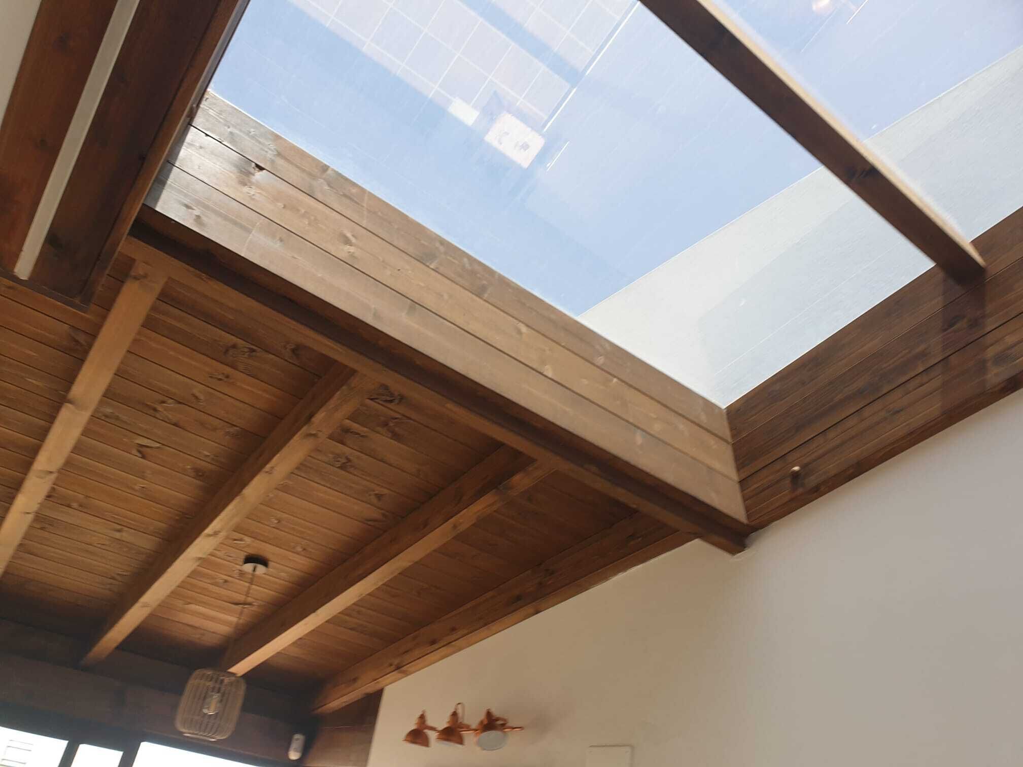 A room with a skylight, wooden beams, and a ceiling fan.