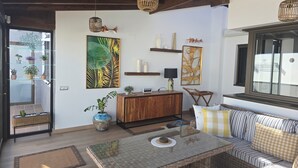 A modern living room with a wooden ceiling, a glass table, a wicker sofa, and a view of the outdoors.