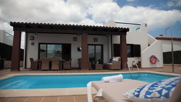 A pool area with lounge chairs, a covered seating area, and a lifebuoy on the wall.