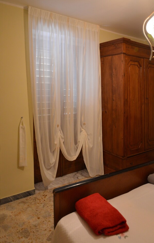 Un dormitorio con un armario de madera, una cama con una toalla roja y una ventana con cortinas de gasa.