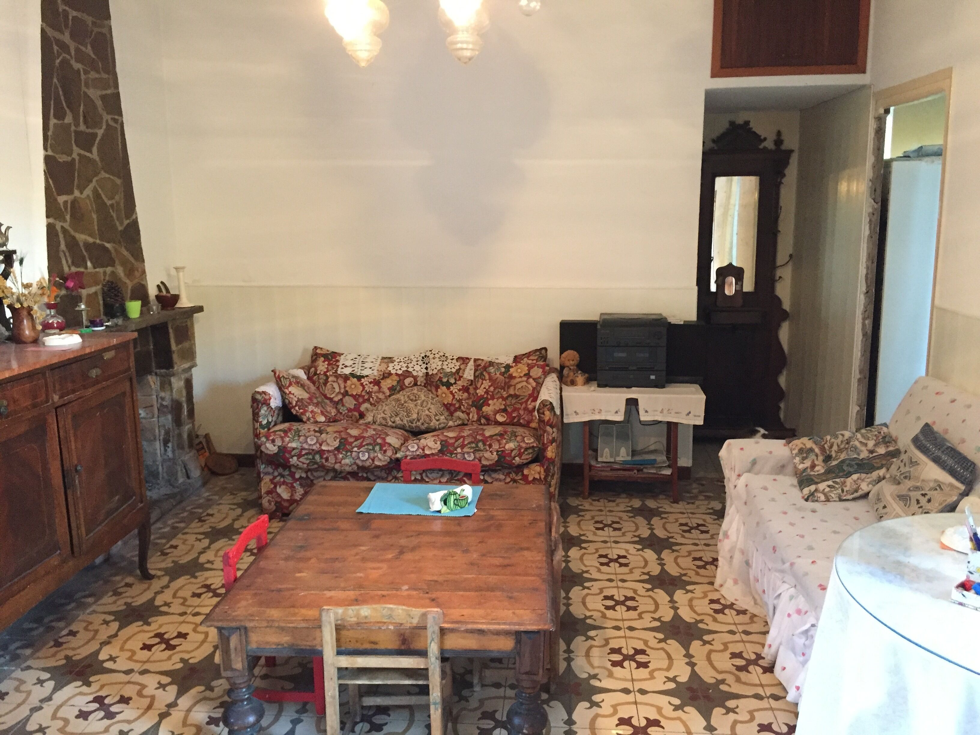 Un salon avec un canapé à motifs floraux, une table basse en bois, un téléviseur posé sur un meuble et un sol à motifs.