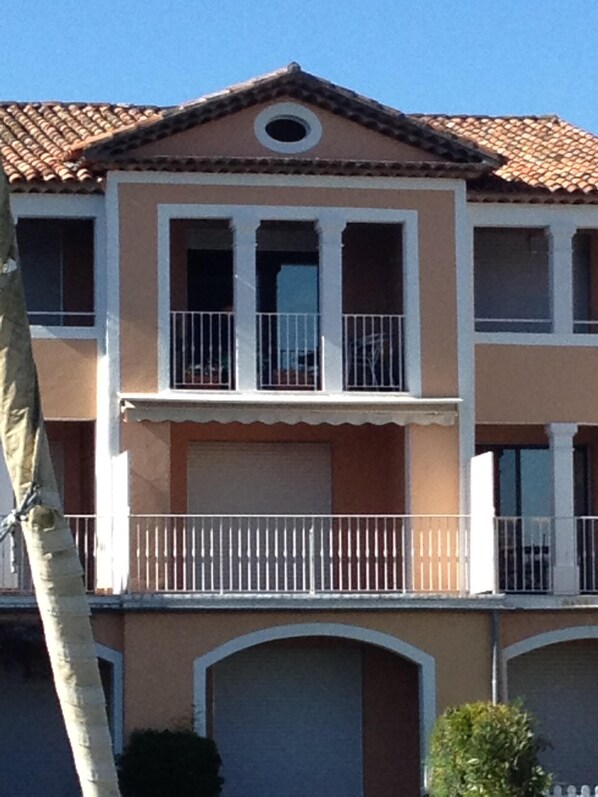 A two-story building with a brown facade, white trim, and a tiled roof. There are balconies with white railings and a garage door. - Romance in Port Grimaud 2p with a/c, parking + private wifi (Grimaud)