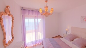 Ein Schlafzimmer mit einem großen Bett, einer Kandelaber, einem Schminktisch mit Spiegel und einem Fenster mit Vorhängen.