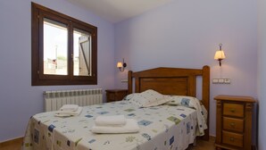 Une chambre à coucher comprenant un lit, deux tables de chevet, une commode, une fenêtre et une lampe fixée au mur.