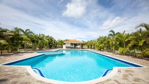 A swimming pool with a tiled deck, surrounded by palm trees and a gazebo.