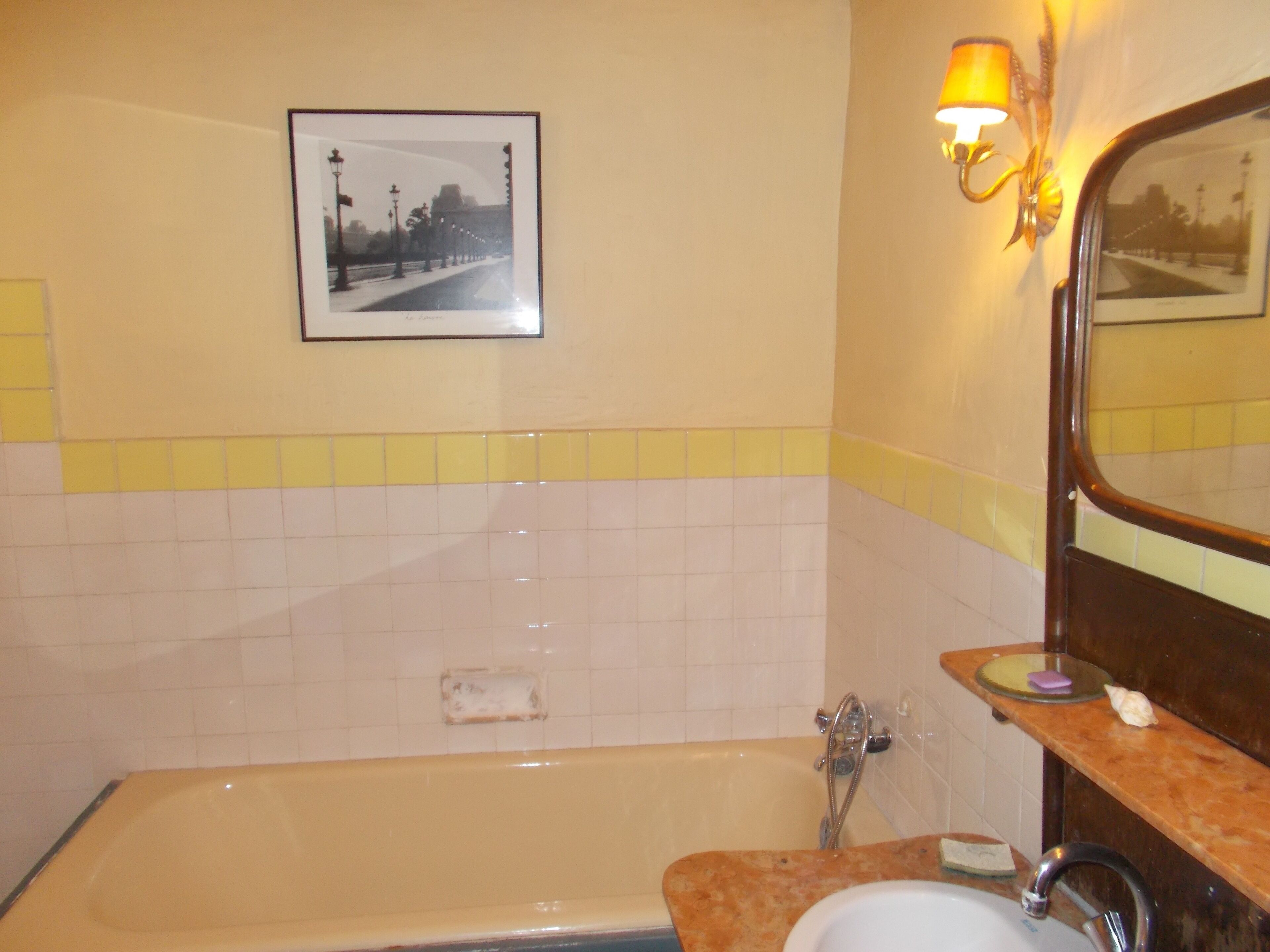 A bathroom with a bathtub, a sink, a mirror, and a wall-mounted picture.