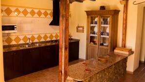 Una cocina con armarios de madera oscura, encimera de granito, microondas y un mueble de madera con puertas de cristal.
