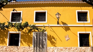 Un edificio amarillo con muros de piedra, múltiples ventanas con barrotes y un farol.