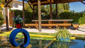 Una pérgola de madera con una mesa de picnic, un columpio de neumático y una fuente decorada con plantas.