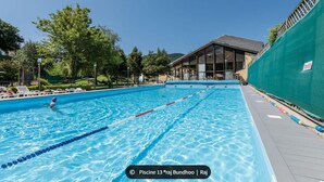 A swimming pool with clear lanes, surrounded by lounge chairs and a building with large windows.