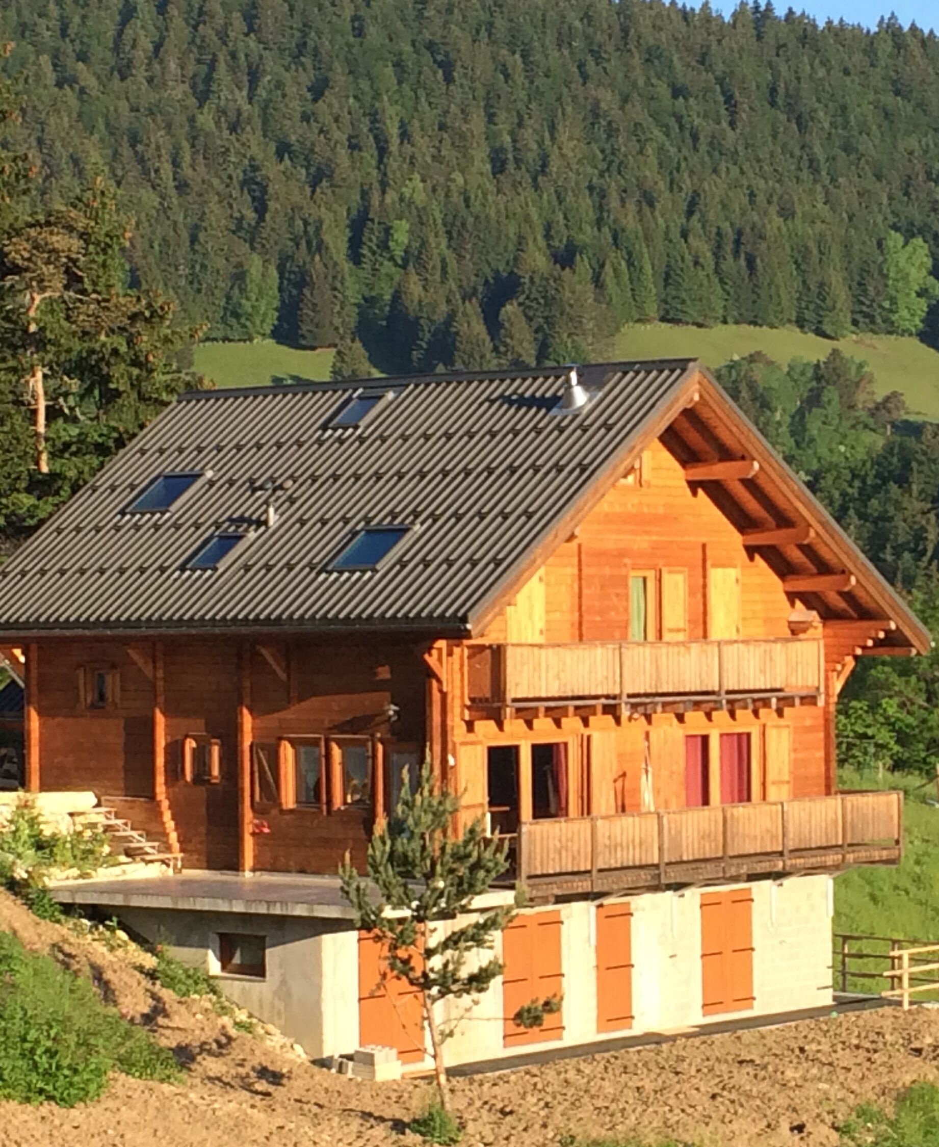 A wooden chalet with a sloped roof, a balcony, and a view of a forested hillside.