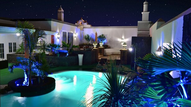 A nighttime pool area with a fountain, palm trees, and a mosque with a minaret.